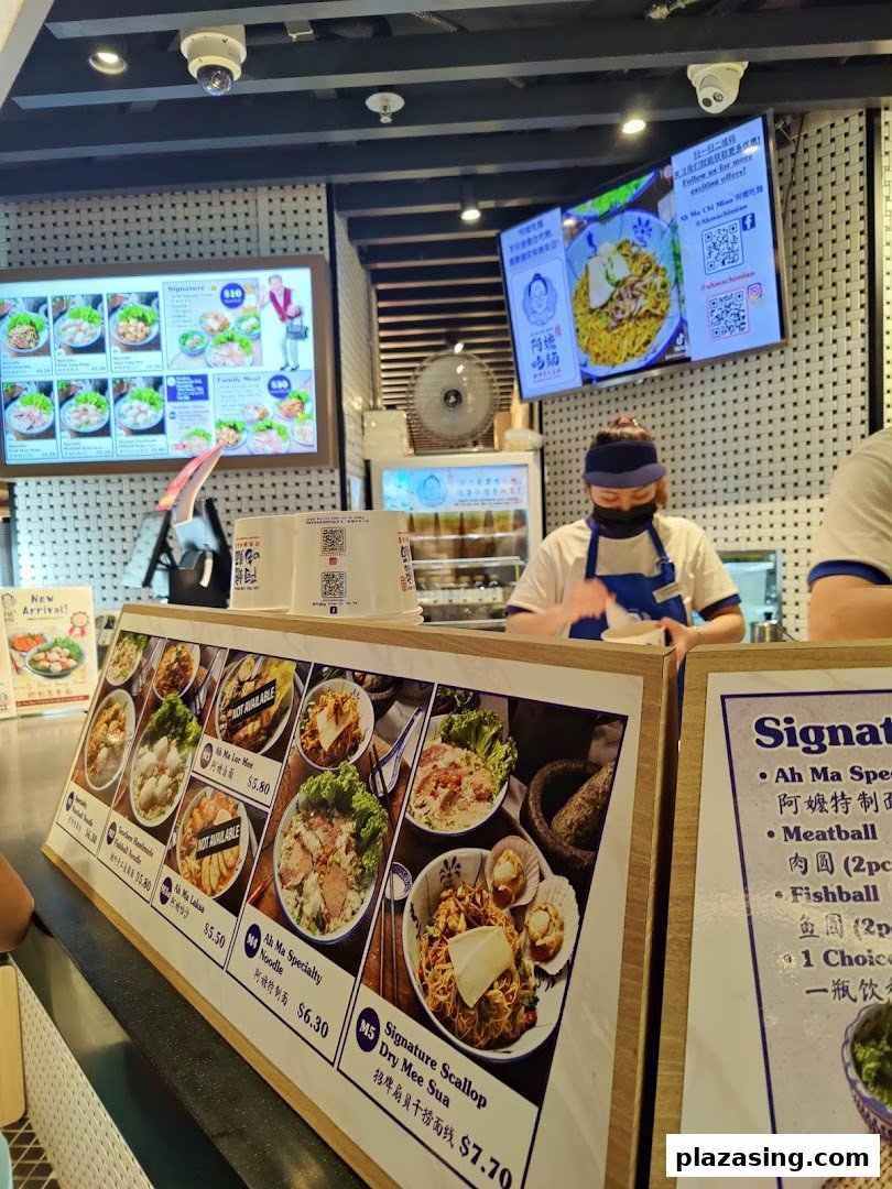 An interior view of Kopitiam Food Hall, featuring a food stall counter with menu displays and a staff member.
