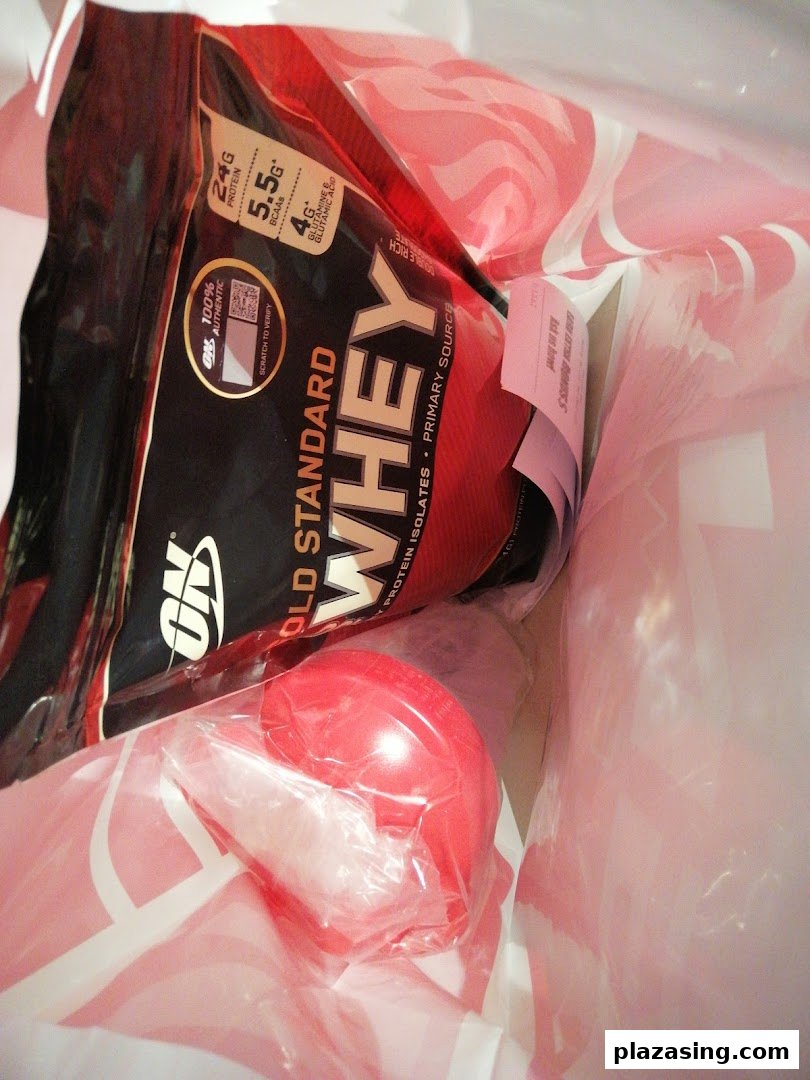 A shopping bag containing Optimum Nutrition Gold Standard Whey protein and a red shaker bottle.