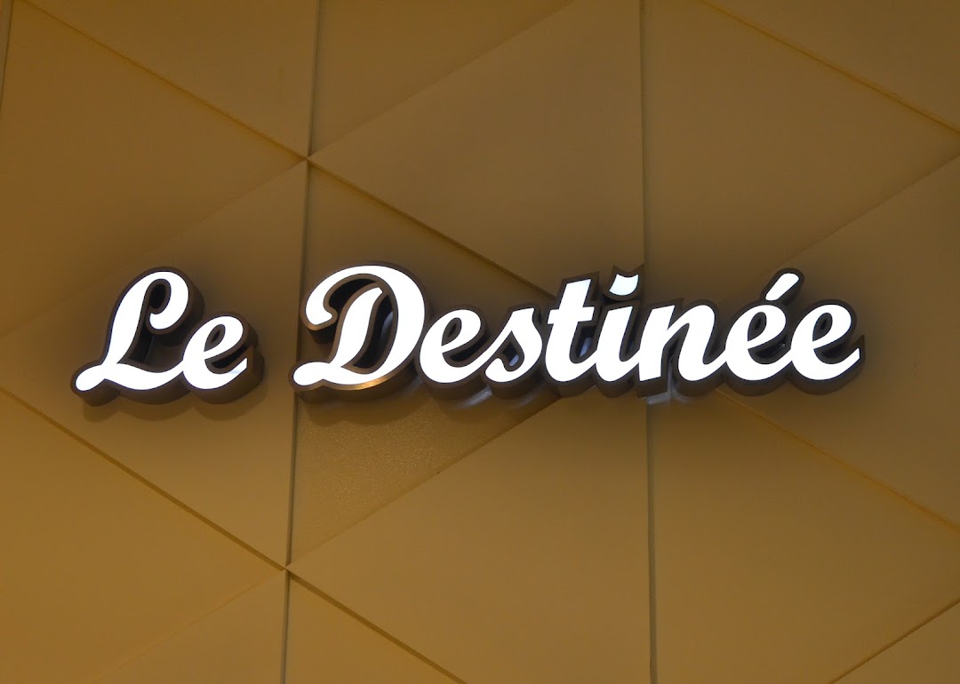 Close-up of the illuminated 'Le Destinee' shop sign on a textured golden wall.