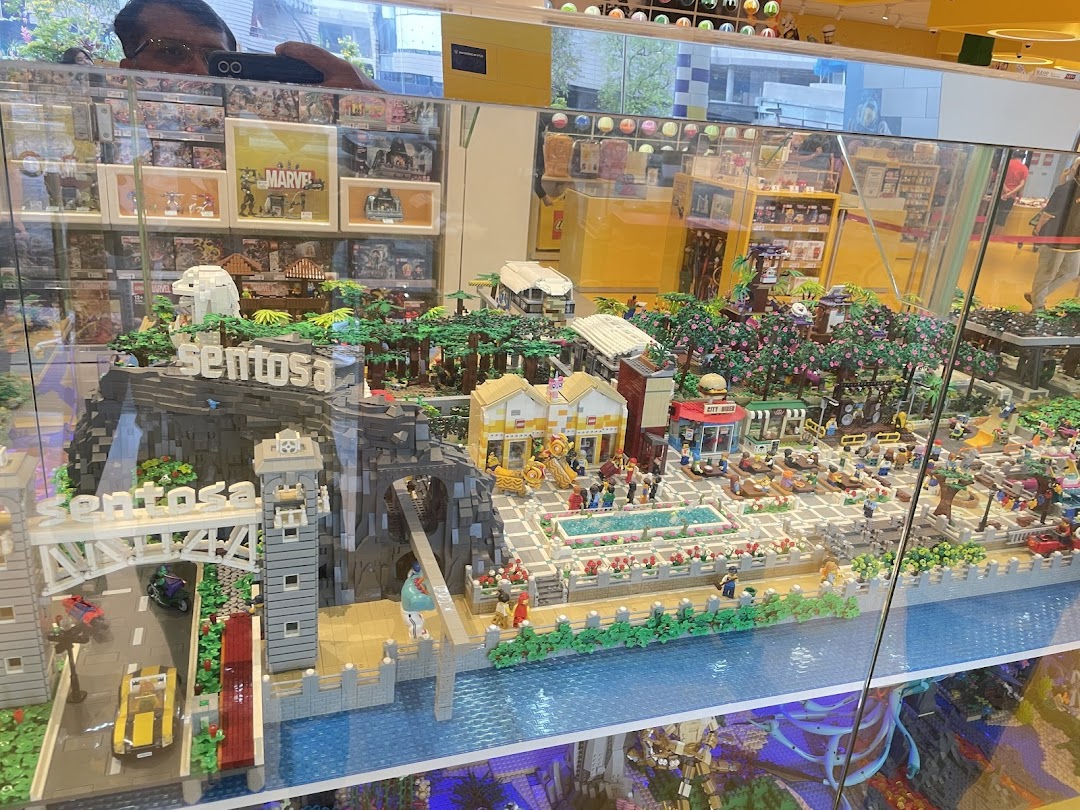 A detailed LEGO model of Sentosa Island, featuring landmarks and vibrant scenes, displayed in a glass case.