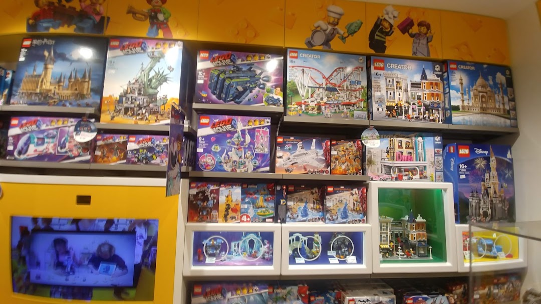 Shelves filled with diverse LEGO sets, including Harry Potter, Creator, and Movie themes, with an interactive display below.
