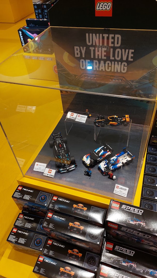 A vibrant LEGO display features racing car models and Technic sets, showcasing the 'United by the Love of Racing' theme.