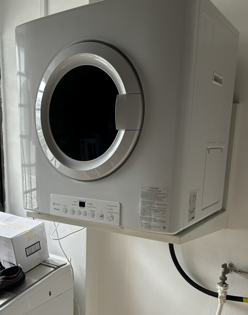 A modern white front-loading dryer or washing machine mounted on a wall.