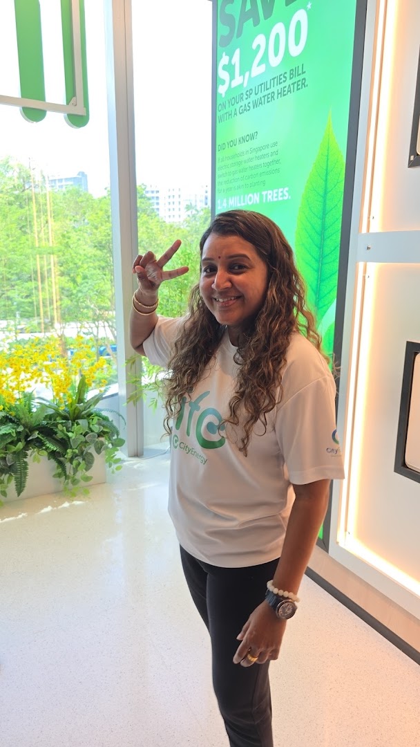 A smiling woman in a 'Life by City Energy' t-shirt makes a peace sign inside the store.