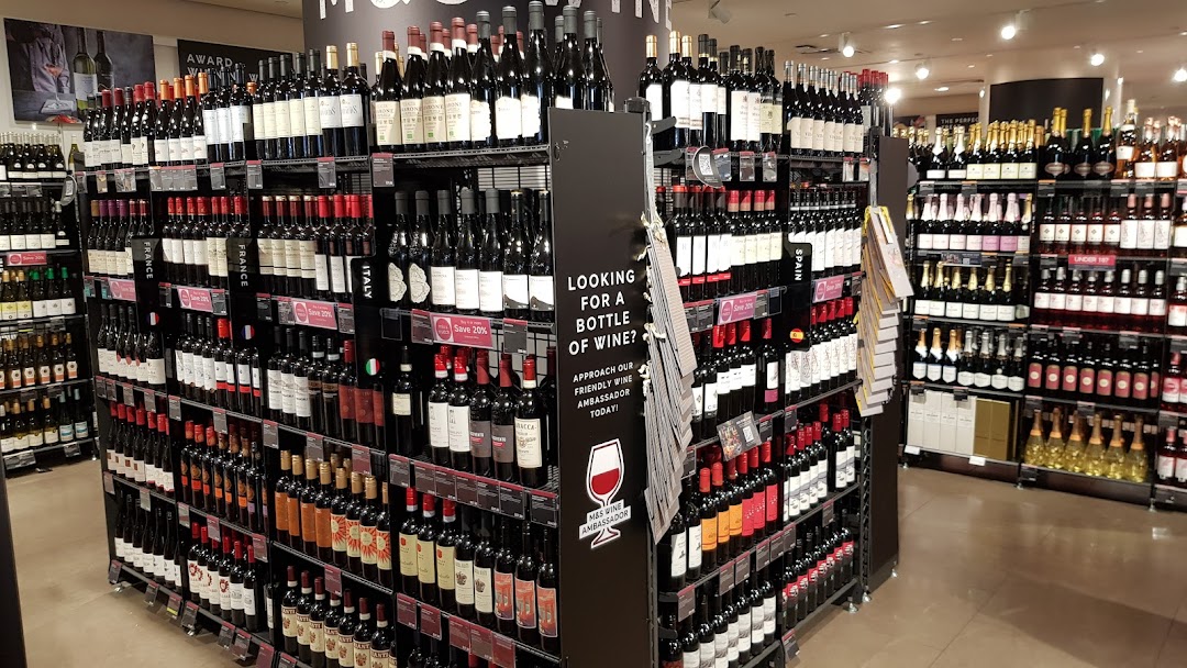 A wide selection of red, white, and sparkling wines displayed on shelves in a Marks & Spencer store.