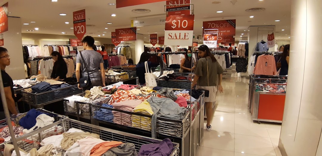 Customers browse clothing racks and sale bins at Marks & Spencer, featuring significant discounts.