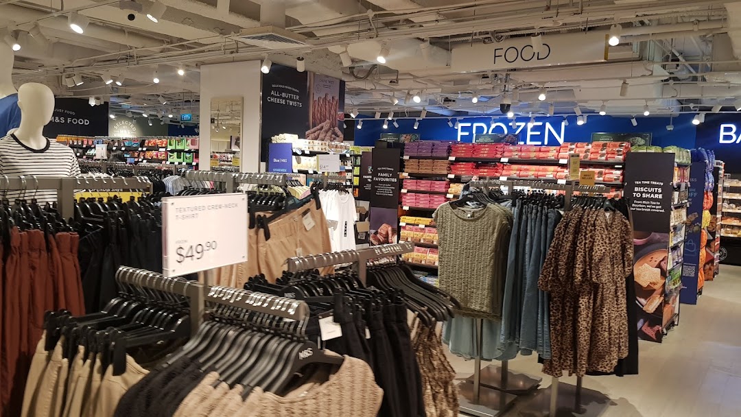 Interior view of Marks & Spencer, showcasing clothing racks and various food sections like frozen and biscuits.