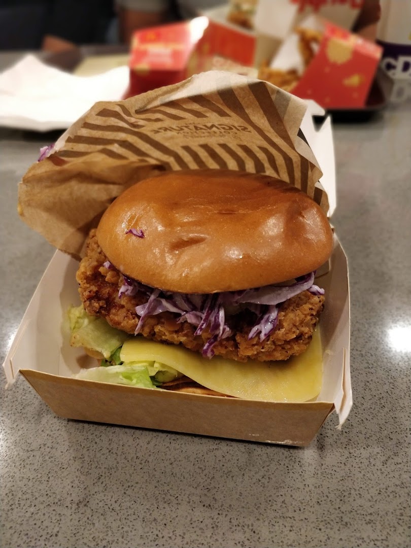 A close-up of a crispy chicken burger with coleslaw and cheese in a McDonald's Signature Collection box.