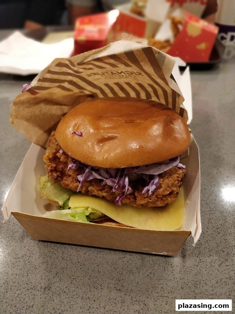 A close-up of a crispy chicken burger with coleslaw and cheese in a McDonald's Signature Collection box.