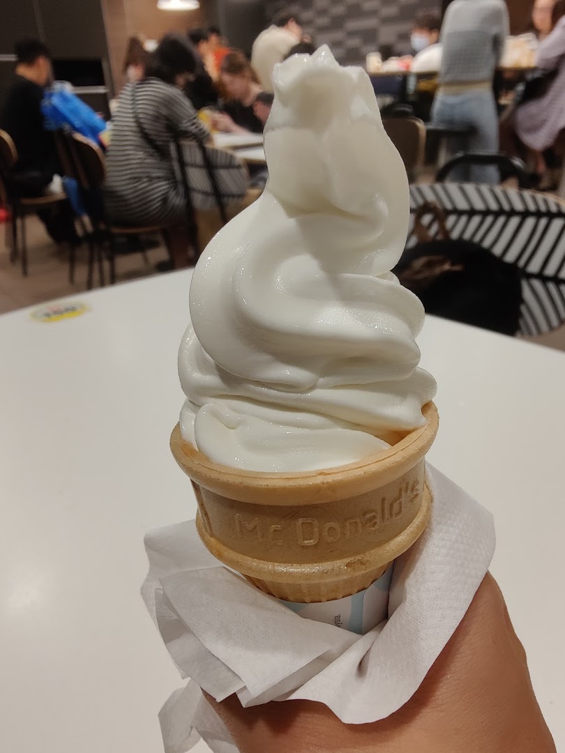 A hand holds a McDonald's soft-serve ice cream cone inside the bustling restaurant.