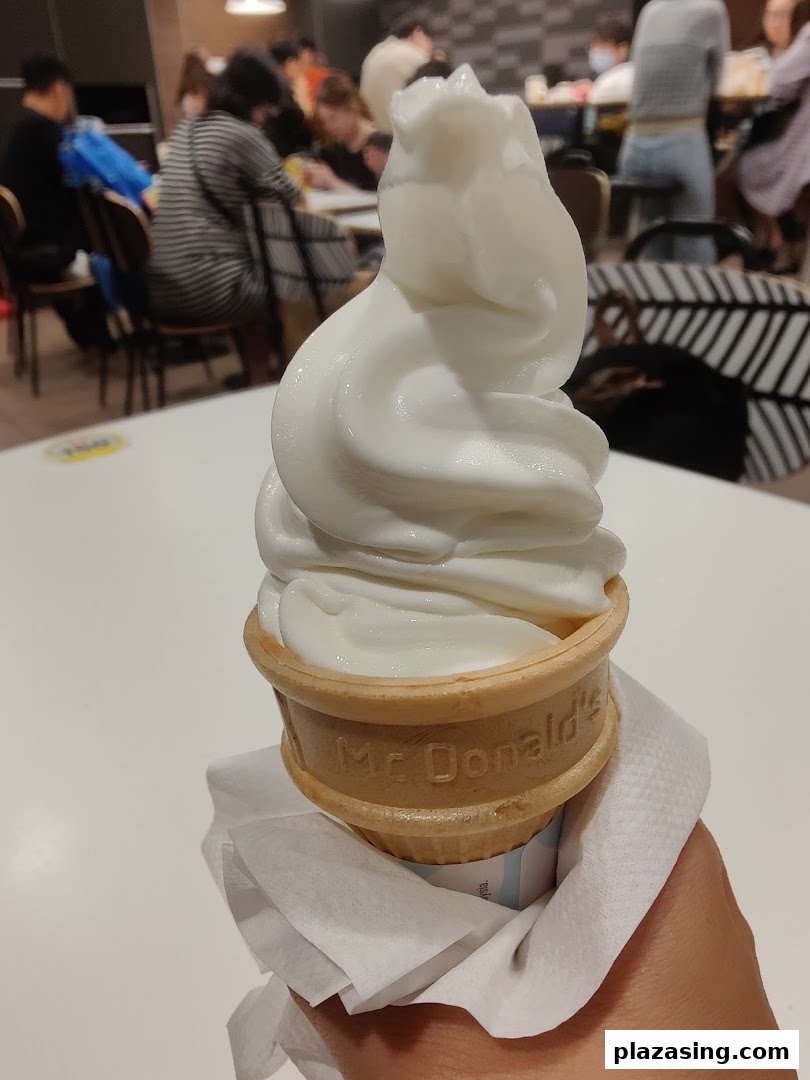 A hand holds a McDonald's soft-serve ice cream cone inside the bustling restaurant.