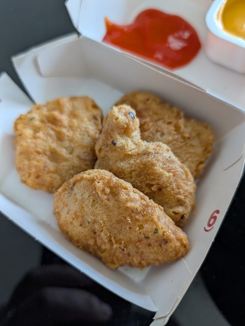 A close-up of golden-brown chicken nuggets in a McDonald's box with ketchup and a dipping sauce.