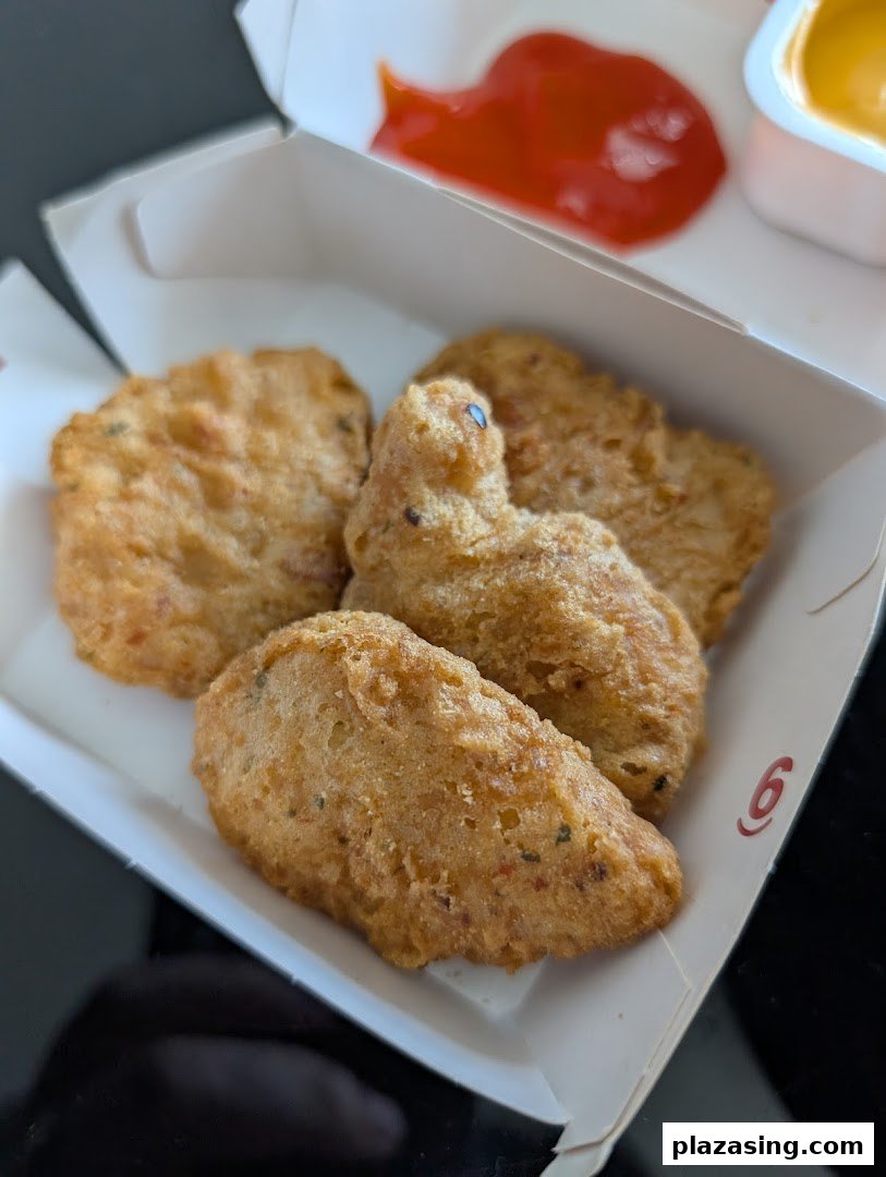 A close-up of golden-brown chicken nuggets in a McDonald's box with ketchup and a dipping sauce.