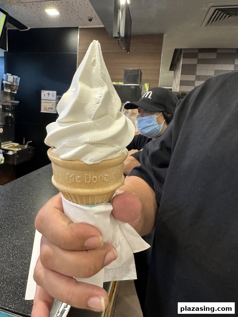 A hand holding a McDonald's soft-serve ice cream cone inside the restaurant, with a staff member in the background.
