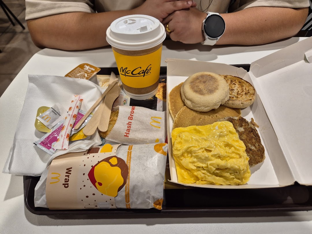 A McDonald's breakfast meal on a tray, featuring pancakes, scrambled eggs, hash brown, and a McCafe drink.
