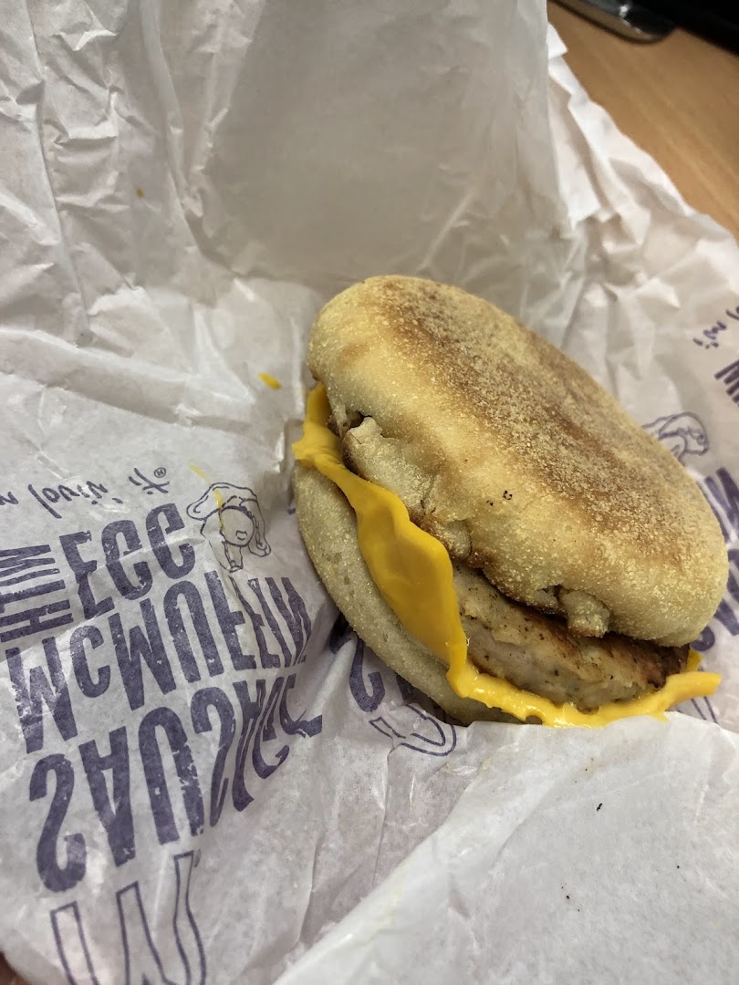 A close-up of a McDonald's breakfast sandwich, likely a Sausage McMuffin with cheese, in its signature wrapper.