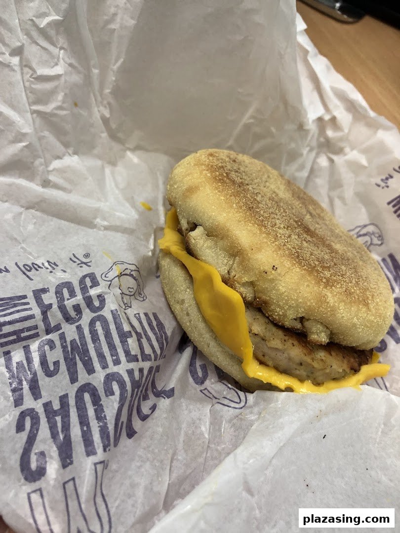 A close-up of a McDonald's breakfast sandwich, likely a Sausage McMuffin with cheese, in its signature wrapper.