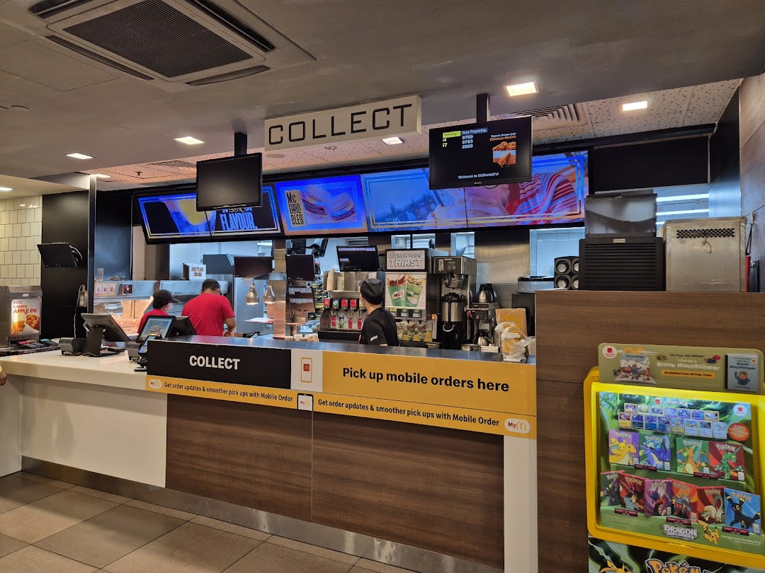 Interior view of McDonald's counter with staff, digital screens, and dedicated order collection points.