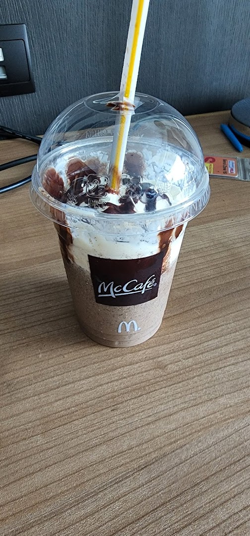 A McCafe chocolate drink with whipped cream and chocolate drizzle on a wooden surface.
