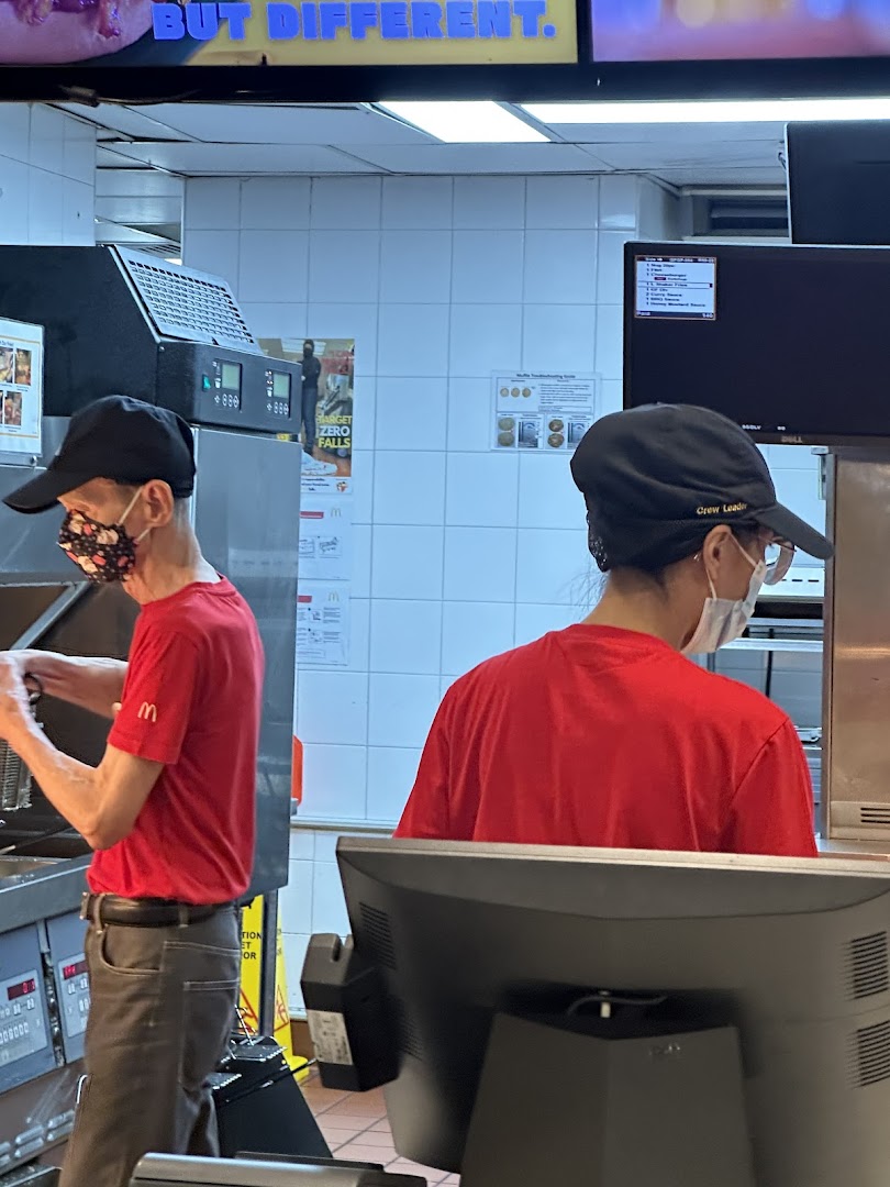 McDonald's staff in red uniforms and masks working diligently in the kitchen area, preparing food.