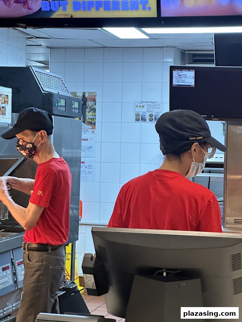 McDonald's staff in red uniforms and masks working diligently in the kitchen area, preparing food.