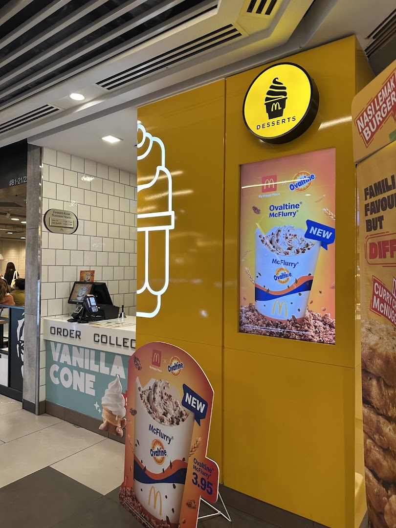 The vibrant yellow dessert counter of McDonald's, featuring promotions for Ovaltine McFlurry and vanilla cones.