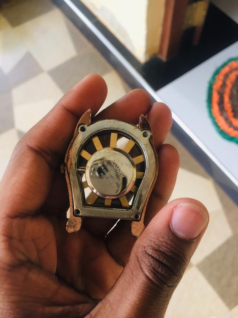 A hand holds the back of a unique watch or accessory, showing its intricate design and brand details.
