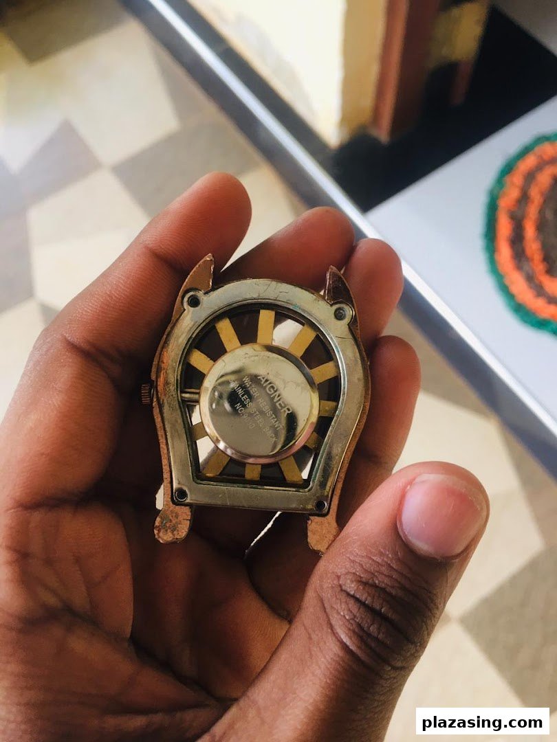 A hand holds the back of a unique watch or accessory, showing its intricate design and brand details.