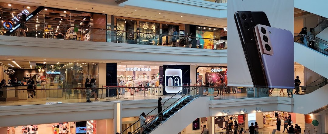 Interior view of Plaza Singapura mall, featuring Mothercare and other retail stores with shoppers and escalators.