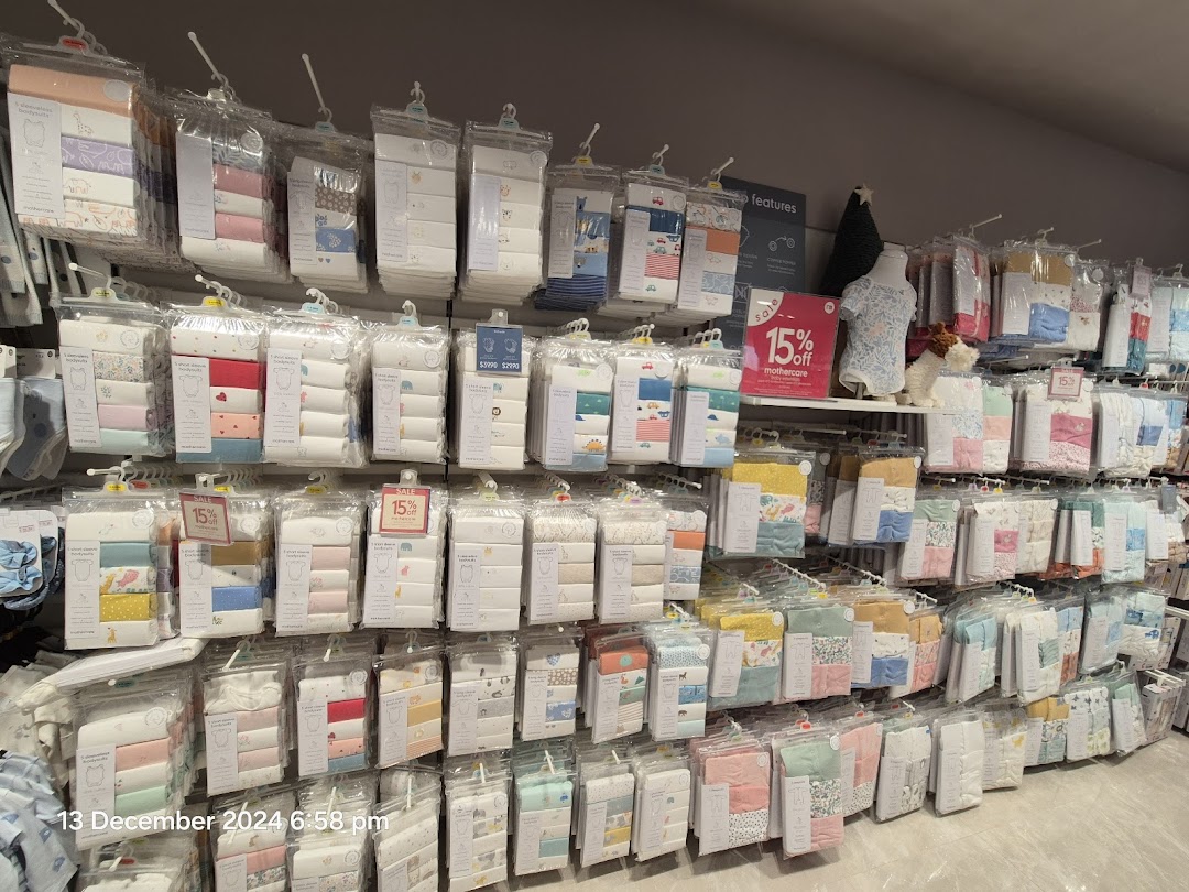 A wide selection of packaged baby clothing, including bodysuits, displayed on racks in a Mothercare store.
