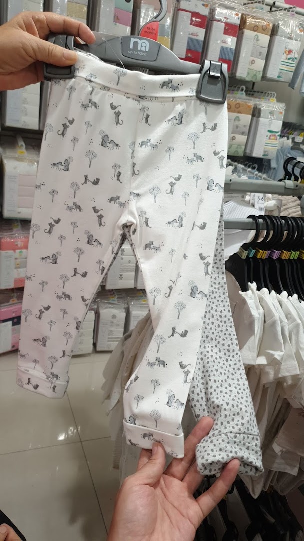 A person holds up white baby leggings with a cute animal print inside Mothercare.