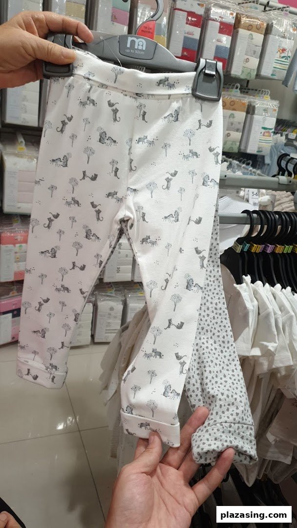 A person holds up white baby leggings with a cute animal print inside Mothercare.
