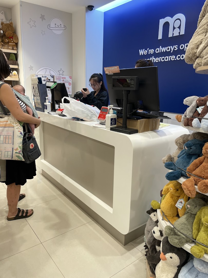 A customer with a baby at the Mothercare cash register, surrounded by baby products and plush toys.