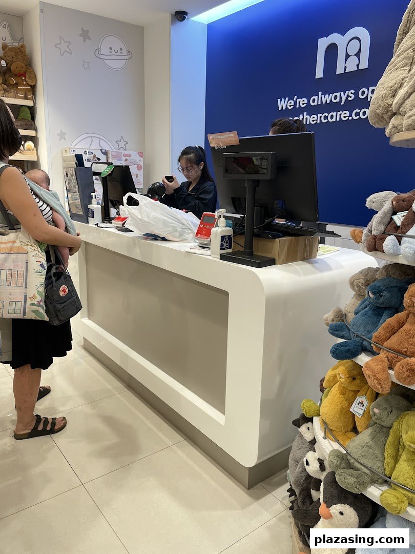 A customer with a baby at the Mothercare cash register, surrounded by baby products and plush toys.