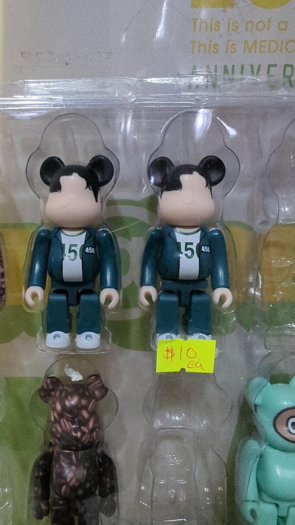 Close-up of collectible figurines, including Squid Game-inspired Bearbricks, displayed in packaging with a price tag.