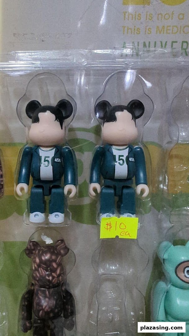 Close-up of collectible figurines, including Squid Game-inspired Bearbricks, displayed in packaging with a price tag.