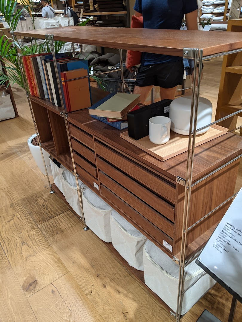 A stylish wooden shelving unit with books, decor, and storage baskets, showcasing Muji's home organization solutions.