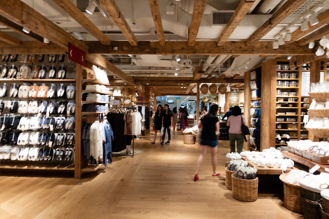 Interior view of MUJI Plaza Singapura, showcasing clothing, household items, and shoppers in a natural wood setting.