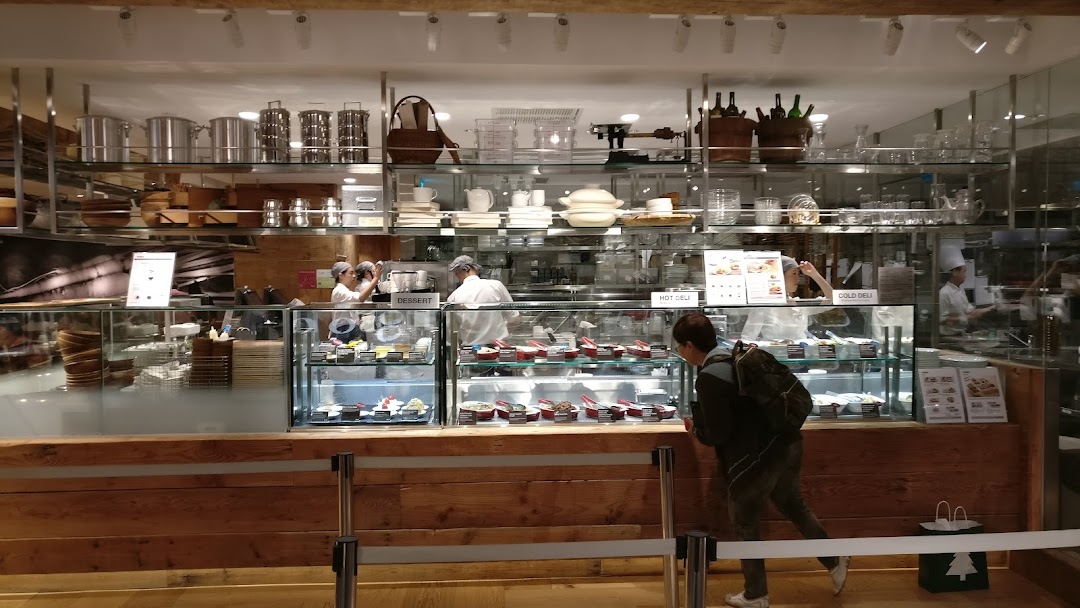 A customer views desserts and deli items at MUJI's in-store cafe counter with staff preparing food.