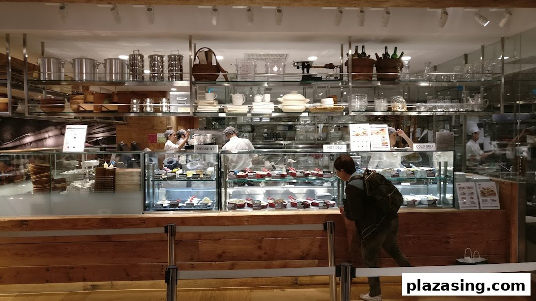 A customer views desserts and deli items at MUJI's in-store cafe counter with staff preparing food.