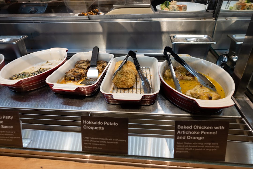 A display of hot prepared dishes including Hokkaido Potato Croquette and Baked Chicken at MUJI.