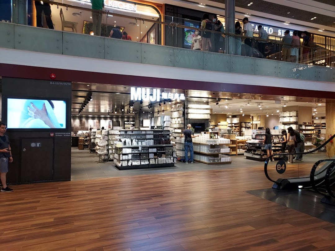 View of MUJI store entrance with interior displays, customers, and a digital screen in a shopping mall.
