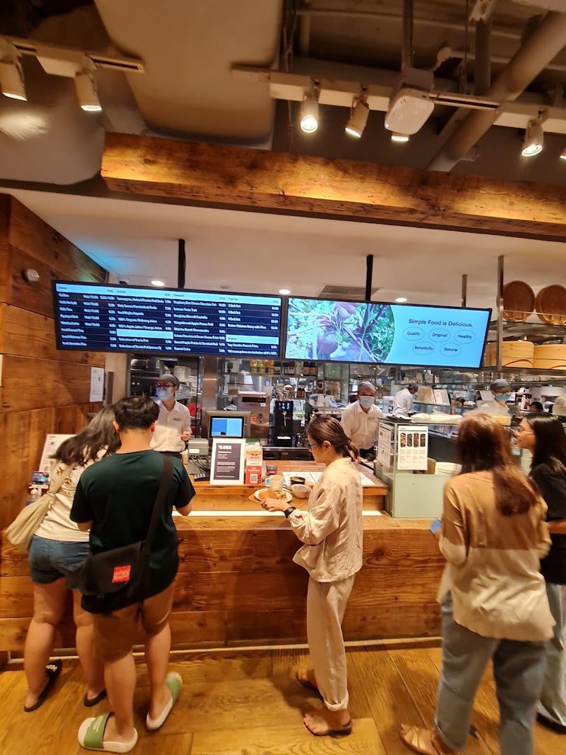Customers ordering at the MUJI Cafe counter with digital menu boards displaying food and drink options.
