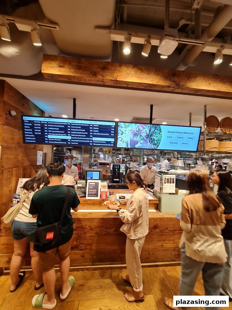 Customers ordering at the MUJI Cafe counter with digital menu boards displaying food and drink options.