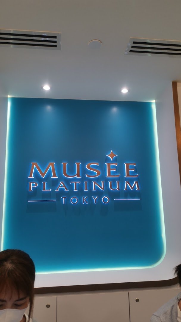 The illuminated Musee Platinum Tokyo logo on a vibrant blue wall inside the shop.