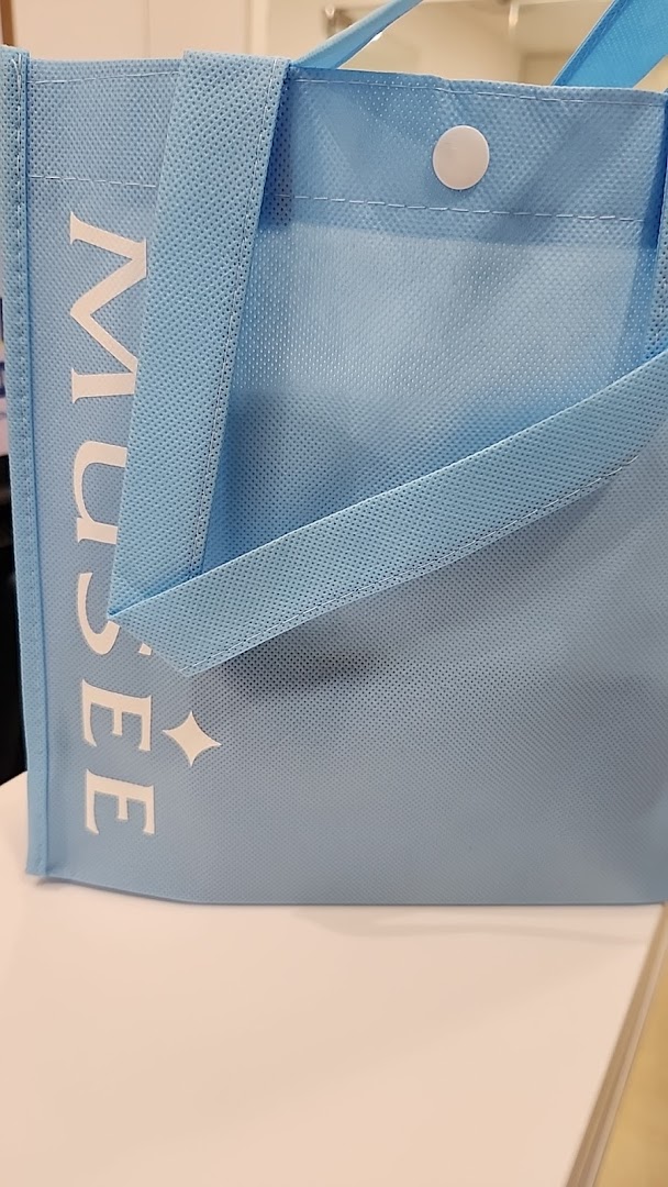 A light blue reusable bag with 'MUSEE' branding and a star-like logo.