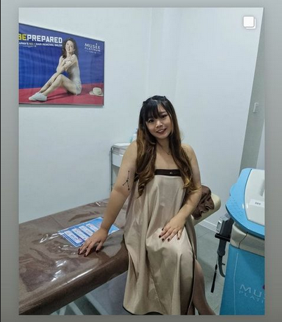 A woman in a treatment room at Musee Platinum Tokyo, featuring a treatment bed and a promotional poster.