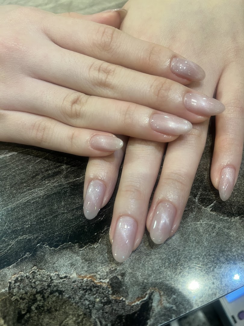 Close-up of hands showcasing elegant, shimmery nude manicured nails on a dark marbled surface.
