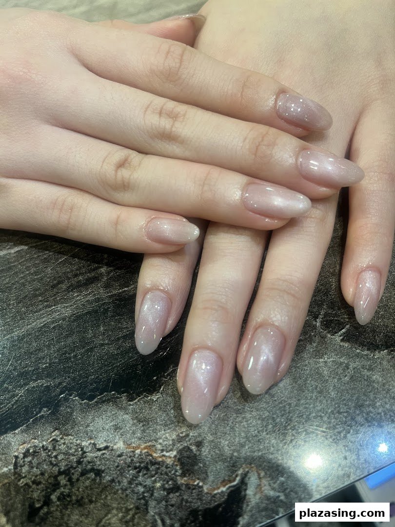 Close-up of hands showcasing elegant, shimmery nude manicured nails on a dark marbled surface.