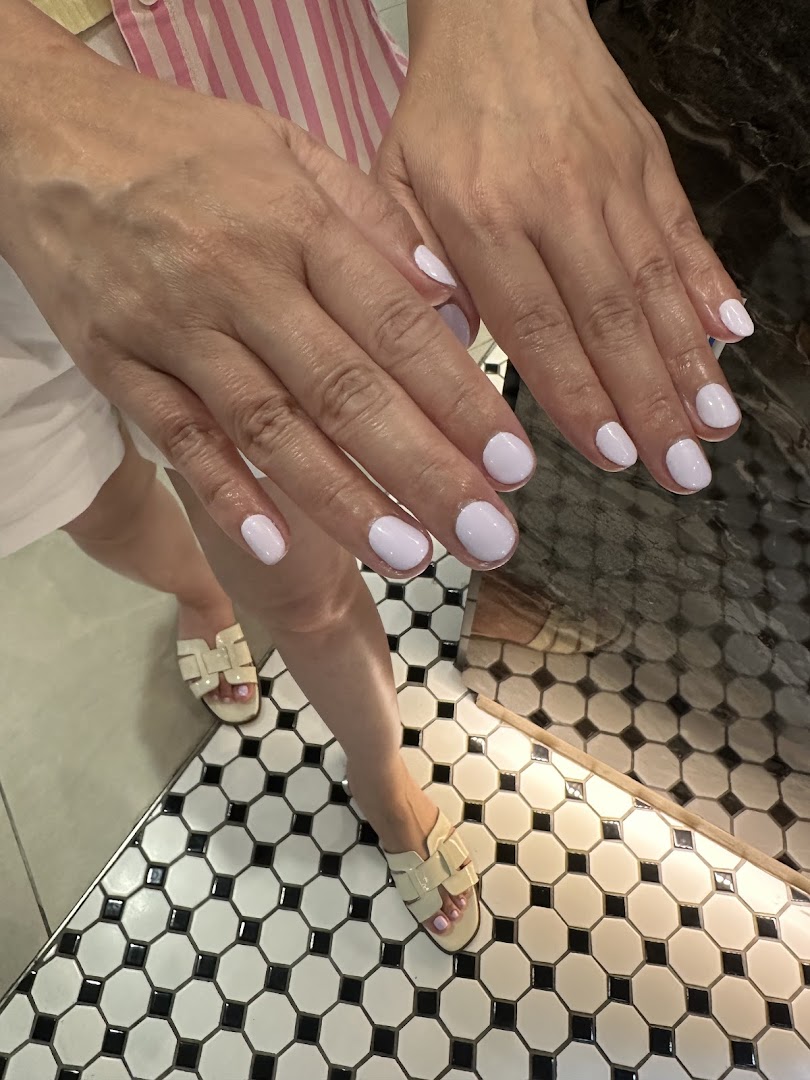 Close-up of hands and feet showcasing freshly painted light purple nails on a stylish tiled floor.